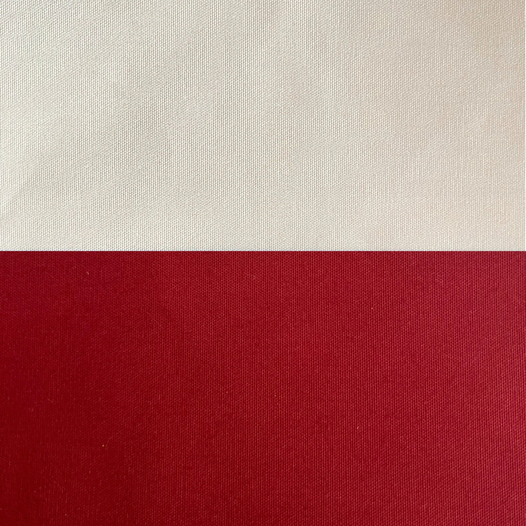 A close-up of a woven fabric or canvas material split horizontally into two color blocks: a warm off-white/cream top section and a deep red bottom section.