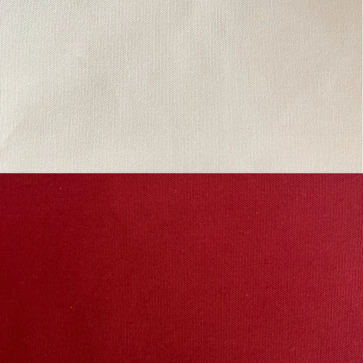 A close-up of a woven fabric or canvas material split horizontally into two color blocks: a warm off-white/cream top section and a deep red bottom section.