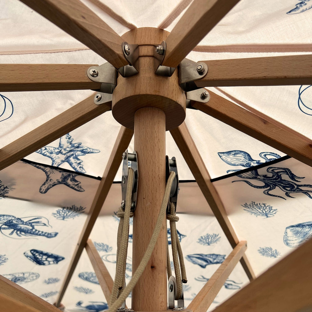 Close-up of a wooden patio umbrella frame with cream fabric canopy printed in blue with starfish, octopus, and shell motifs.
