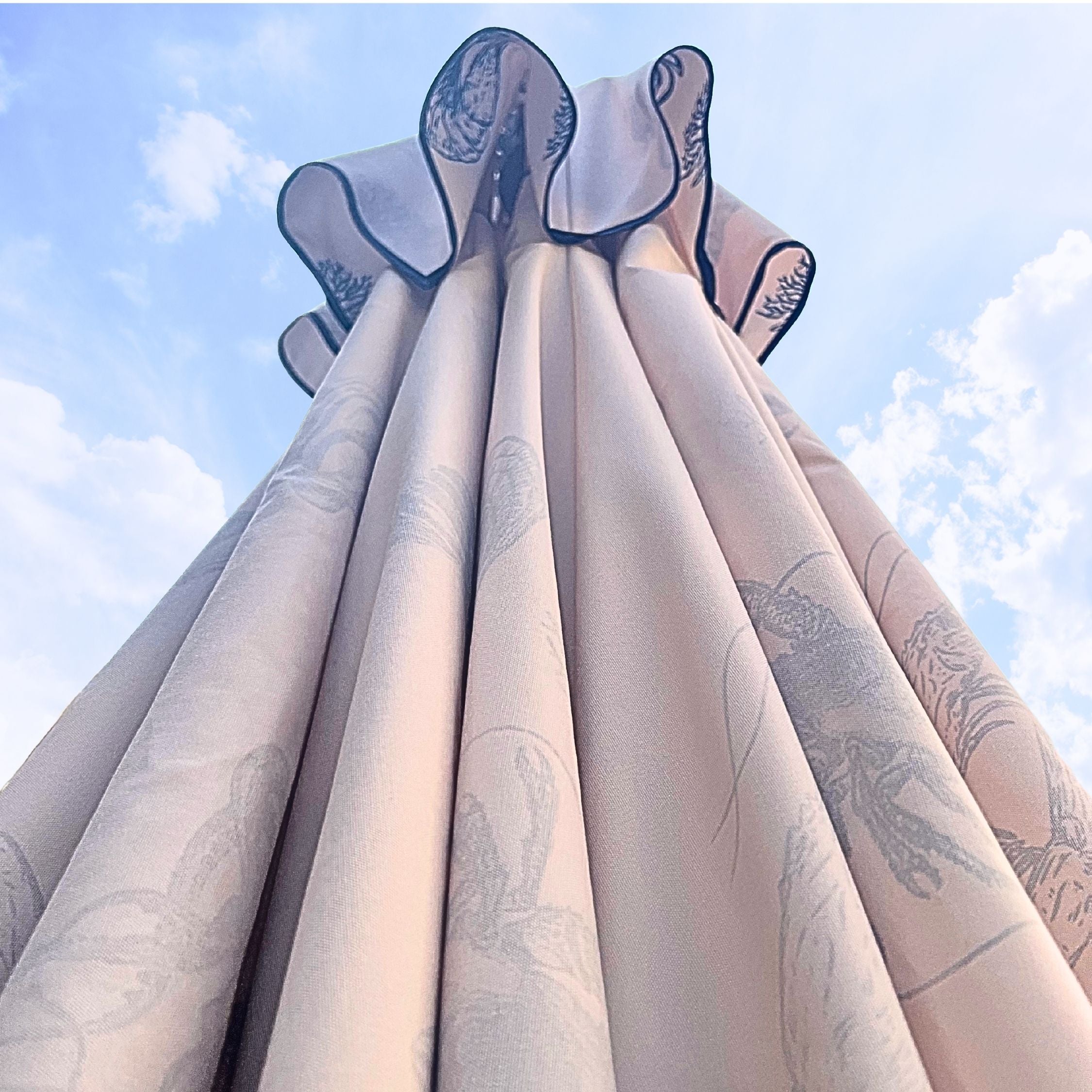 A close-up, low-angle view of a cream canvas parasol canopy with navy piping around the air vent section,  set against a blue sky with clouds.