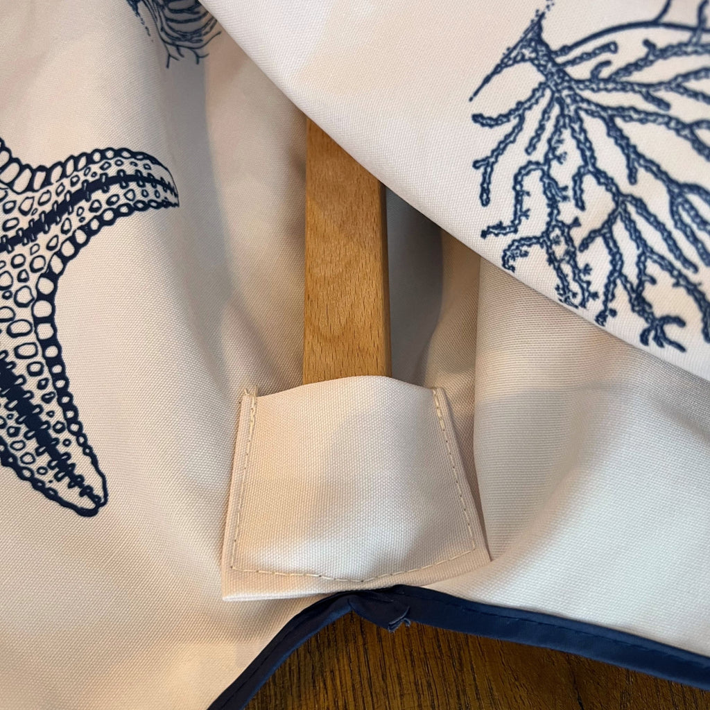Close-up of a cream coloured fabric parasol canopy with navy blue nautical prints, showing one of the hardwood frame rods tucked into the high quality stitched pocket that houses it