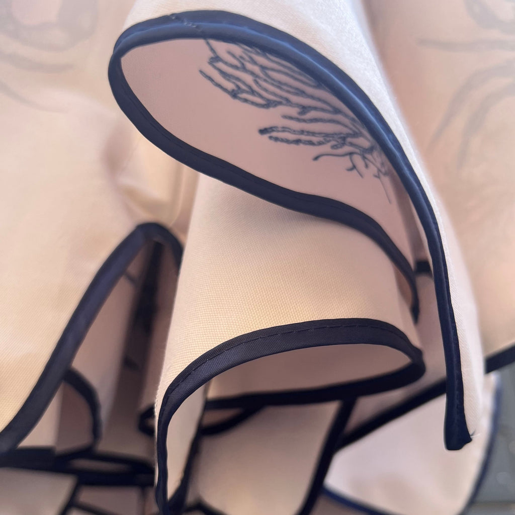 A close-up of a parchment cream parasol canopy with detail of navy piping . A view of the inside of the canopy reveals various hand-drawn maritime motifs