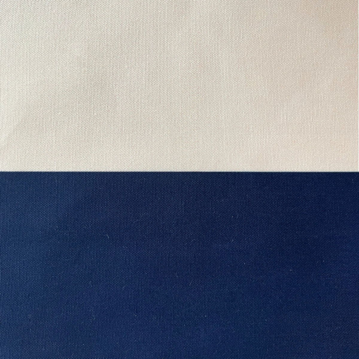 A close-up of a fabric or material swatch split horizontally into two color blocks: a warm off-white/cream section on top and a deep navy blue section on the bottom.