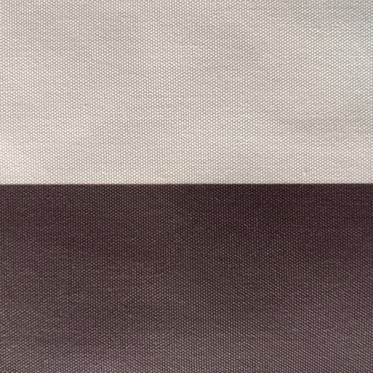 A close-up of a woven fabric texture split horizontally into two solid sections: a light warm gray/beige on top and a dark charcoal gray on the bottom.